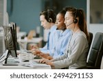 Young biracial call center operators sitting at work desk with electronic devices and office supplies on top in modern and cozy office