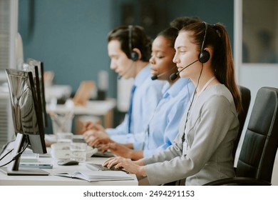 Young biracial call center operators sitting at work desk with electronic devices and office supplies on top in modern and cozy office