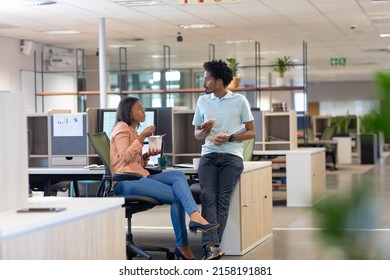 Young biracial colleagues discussing while eating lunch together in cubicle at modern workplace. unaltered, business, food, teamwork and modern office concept.