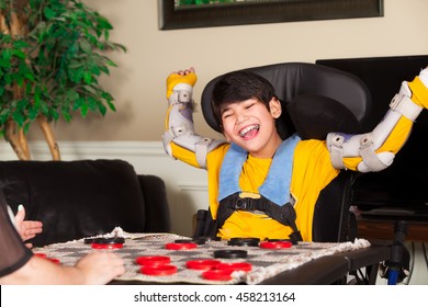 Young biracial disabled boy in wheelchair playing checkers at home. Child has cerebral palsy.