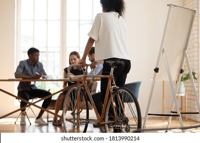 Young Biracial Female Employee Ride Bicycle In Modern Office, Back View Of African American Woman Worker Test Try New Bike, Colleagues Brainstorm Discuss Business Ideas, Stress Free Concept