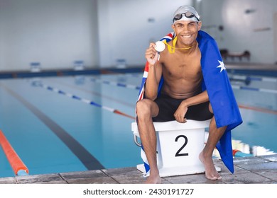 Young biracial male swimmer celebrates at the poolside, draped in an Australia flag with a medal. His victory at a swimming competition brings pride and joy. - Powered by Shutterstock