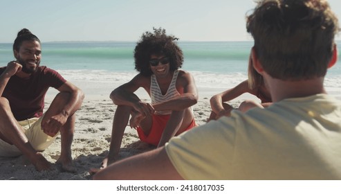 Young biracial man and friends enjoy a sunny beach day, with copy space. Laughter and conversation fill the air as they relax on the sandy shore. - Powered by Shutterstock