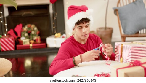 Young biracial man wrapping gifts at home, with copy space. He is preparing for the festive season in a cozy living room setting. - Powered by Shutterstock