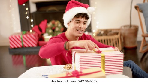 Young biracial man wrapping gifts at home, with copy space. He's preparing presents with festive decorations around him. - Powered by Shutterstock