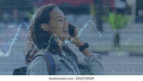 Young biracial professional wearing casual clothes, laughing on phone. She has long dark hair, wearing light makeup, with stock market graphics overlay - Powered by Shutterstock