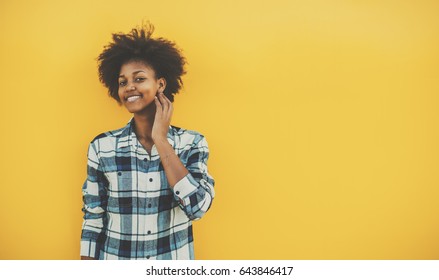 Young biracial student girl with perfect smile and curly afro hair in casual checkered outfit staying in front of solid yellow wall and touching her face, with copy space place for your advertising - Powered by Shutterstock