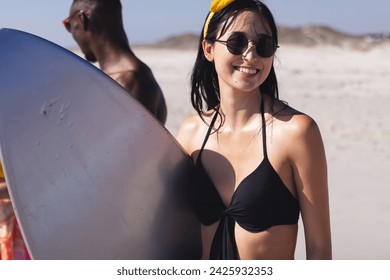 Young biracial woman and African American man enjoy the beach. They carry a surfboard, ready for a day of water sports in the sun. - Powered by Shutterstock