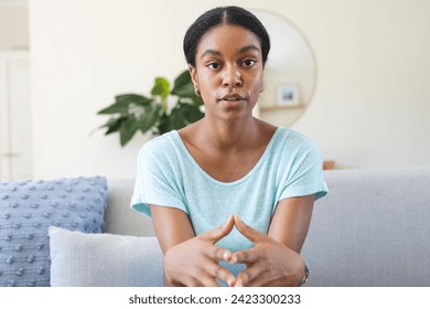 Young biracial woman sits thoughtfully in a home setting on a video call. Her expression suggests contemplation or a moment of decision-making. - Powered by Shutterstock