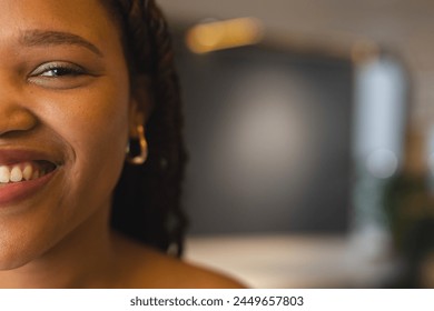 Young biracial woman smiling, wearing gold hoop earrings in a modern business office with copy space. She has braided hair, brown eyes, and a joyful expression, unaltered. - Powered by Shutterstock