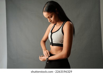 Young biracial woman in sportswear adjusting fitness tracker watch in studio - Powered by Shutterstock