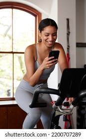 Young Biracial Woman Using Mobile Phone While On Exercise Bike At The Gym