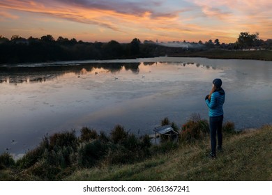Young birdwatcher woman standing with binoculars near the pond in the evening. Birdwatching hobby background image