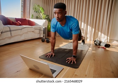 Young Black African American Male Working Out At Home Holding A Plank Position About To Do Push Ups On A Yoga Mat. Following An Online Class Using His Laptop.