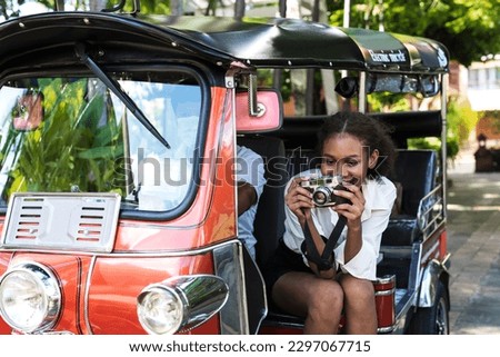 Young black African American traveller sitting besise Tuktuk car and taking picture during summer vacation in Chiangmai Thailand, independent female tourist sitting in local tuk tuk explore Chiangmai