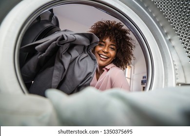 Young black African American woman holding a basket of clothes to be washed in a automatic laundry