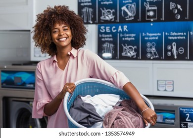 Young black African American woman holding a basket of clothes to be washed in a automatic laundry - Translated text : Dry