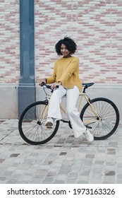 Young black african american woman on a cool yellow fixie bike in front of pink brick wall