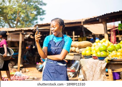 young black African businesswoman using her mobile phone in a local market excited After using receiving Good news 