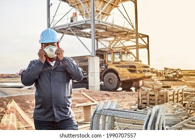 A Young Black African Coal Mine Worker Wearing Coveralls And Hard Hat Putting On Face Mask After A Long Day Of Work On Site At The Coal Mine