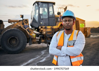A young Black African coal mine foreman looking into camera wearing reflective bib and hard hat after a long day of work on site at the coal mine