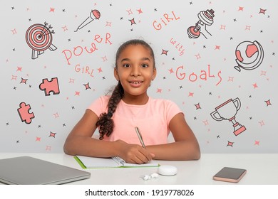 A Young Black African Girl With A Rapturous Look Is Writing Down Her Goals In A Notebook.  Doodle About Powers Of The Girl Are Drawn On The Background. Happy Childhood Concept