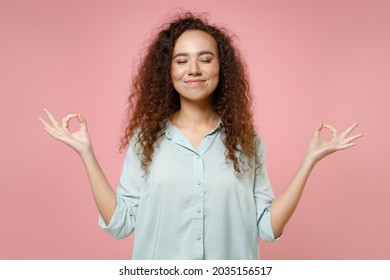 Young black african happy curly spiritual woman 20s wearing blue casual shirt hold spreading hands in yoga om gesture relax meditate try to calm down isolated on pastel pink background studio portrait
