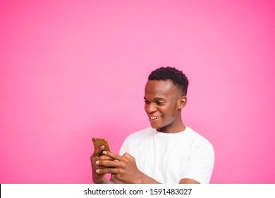 ピンクのスタジオの壁に立っている若い黒人男性。携帯電話を使って、オンラインで笑顔を見ながら、面白い内容をチェックしている。技術と反応のコンセプト写真素材1591483027  | Shutterstock