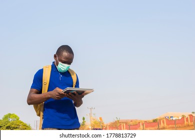 Young Black African Man Student Carrying Schoolbag Wearing Face Mask Checking Internet Using Tablet .black African University Student Wearing Nose Mask Chatting With Friends On Social Media