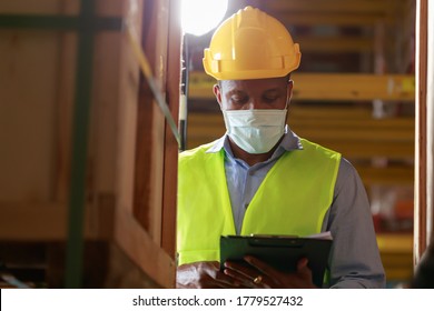 Young Black African Worker Wearing Protective Face Mask Working In Factory Warehouse. Black Man Checking Stock, New Normal After Covid 19 Pandemic Crisis. Logistic Industry Concept.