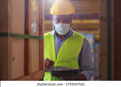 Young Black African Worker Wearing Protective Face Mask Working In Factory Warehouse. Black Man Checking Stock, New Normal After Covid 19 Pandemic Crisis. Logistic Industry Concept.