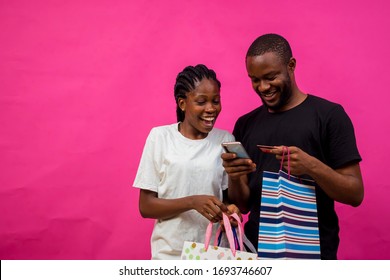 Young Black Beautiful Lady Holding Some Shopping Bags With A Black Guy Making Card Payment On His Phone