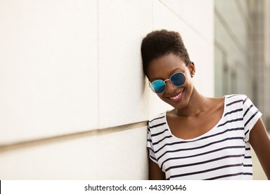 young black beautiful woman smiling next to a wall with sunglasses and striped shirt - Powered by Shutterstock