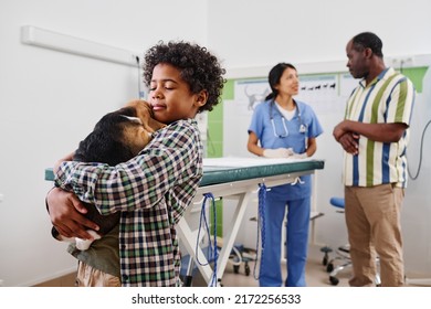 Young Black boy tenderly hugging his pet after medical checkup, while his father and vet discussing something