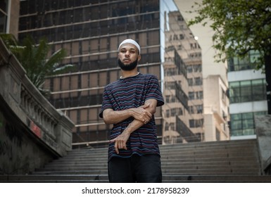 Young Black Brazilian Man With Beard, Striped T-shirt, Bag, Durag, Ring And Pearl Chain Standing On The Stairs In Downtown São Paulo