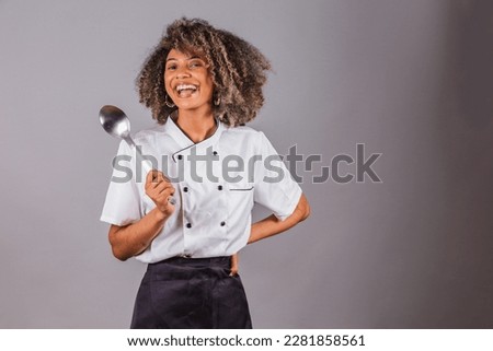 Young black Brazilian woman, cook, masterchef, wearing restaurant uniform. holding big spoon for preparing sauces.
