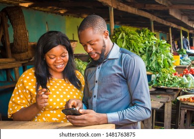 Young Black Business Agent Meeting With A Woman Selling In A Local Market, Showing Her Something On His Phone