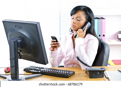 Young Black Business Woman Multitasking Using Two Phones In Office