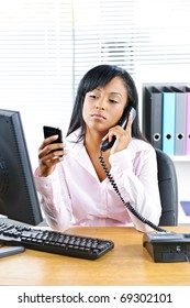 Young Black Business Woman Multitasking Using Two Phones In Office