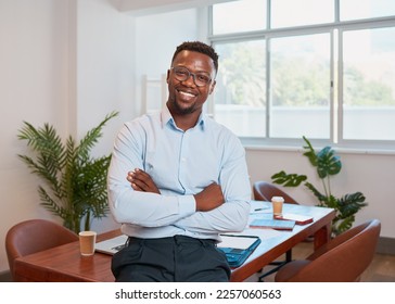 A young Black businessman poses with arms folded at conference table in office