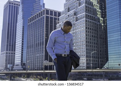 A Young Black Businessman Is Standing In A Business District, Looking Down And Into Deeply Thinking.