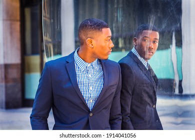 A young black businessman is standing by a mirror on the street and looking at the reflection. Concept of self assured, self esteem and self checking. A fine art lifestyle color photography.