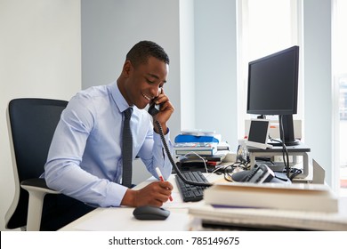 Young Black Businessman Using The Phone At His Office Desk