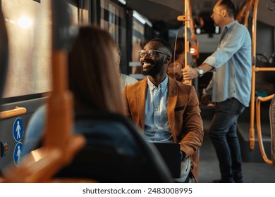 Young black businessman wearing eyeglasses smiling on a public bus while sitting with a laptop on his lap. - Powered by Shutterstock