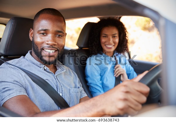 Young black couple in a car on a road trip smiling\
to camera