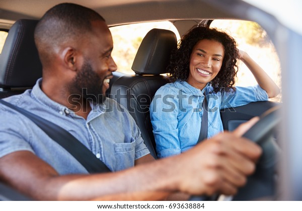 Young black couple in car on road trip smiling at\
each other