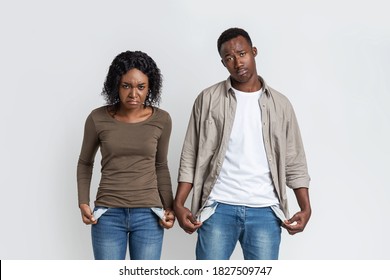 Young Black Couple With Empty Pockets And No Money Over Grey Studio Background, Upset African American Man And Woman Showing Their Empty Pockets, Suffering From Financial Problems During Lockdown