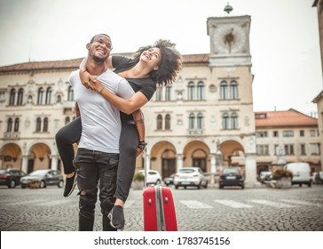 Young Black Couple Hugged And Happy With The Travel Bag In An Italian City. Black Tourists In Italy