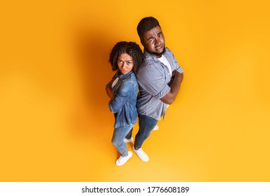 Young Black Couple Looking Suspiciously At Camera In Disbelief, Standing Back To Back Over Yellow Background, Top View