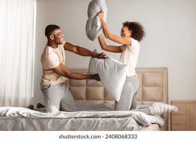 Young black couple playfully engages in a pillow fight, laughing with joy while having fun together on carefree morning, in modern home bedroom, fighting holding pillows - Powered by Shutterstock